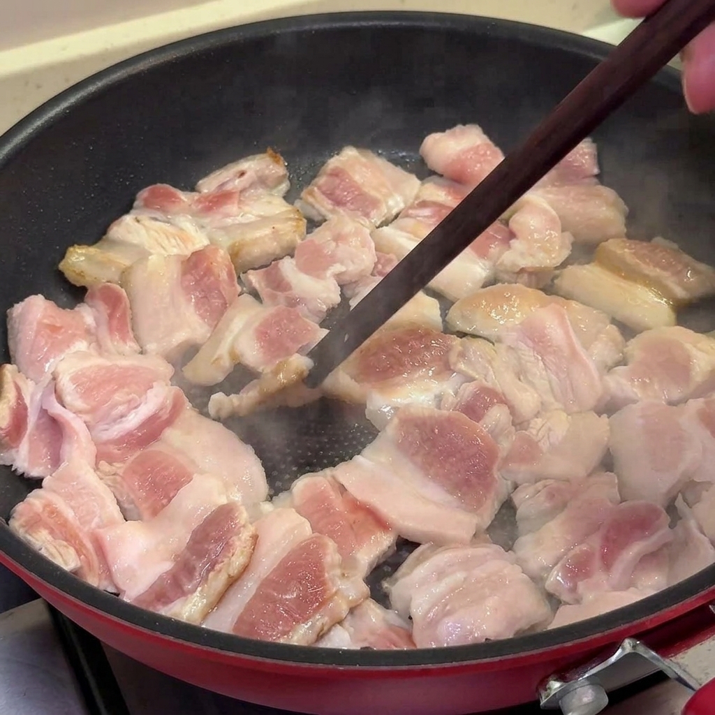 Schweinebauchscheiben werden in einer beschichteten Pfanne goldbraun und leicht knusprig gebraten und mit Essstäbchen gewendet.