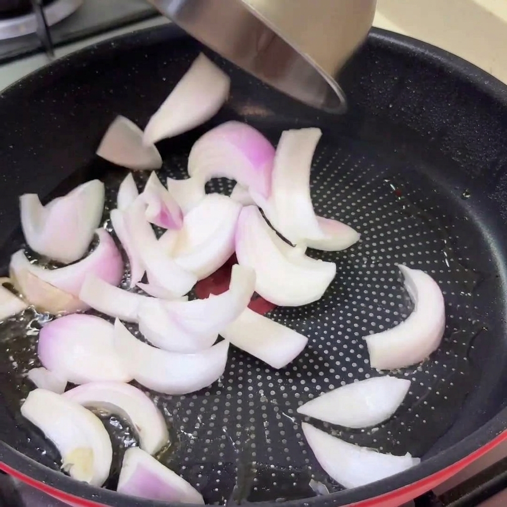 In Streifen geschnittene rohe Zwiebeln werden aus einer Schüssel in eine heiße Pfanne mit Öl gegeben.