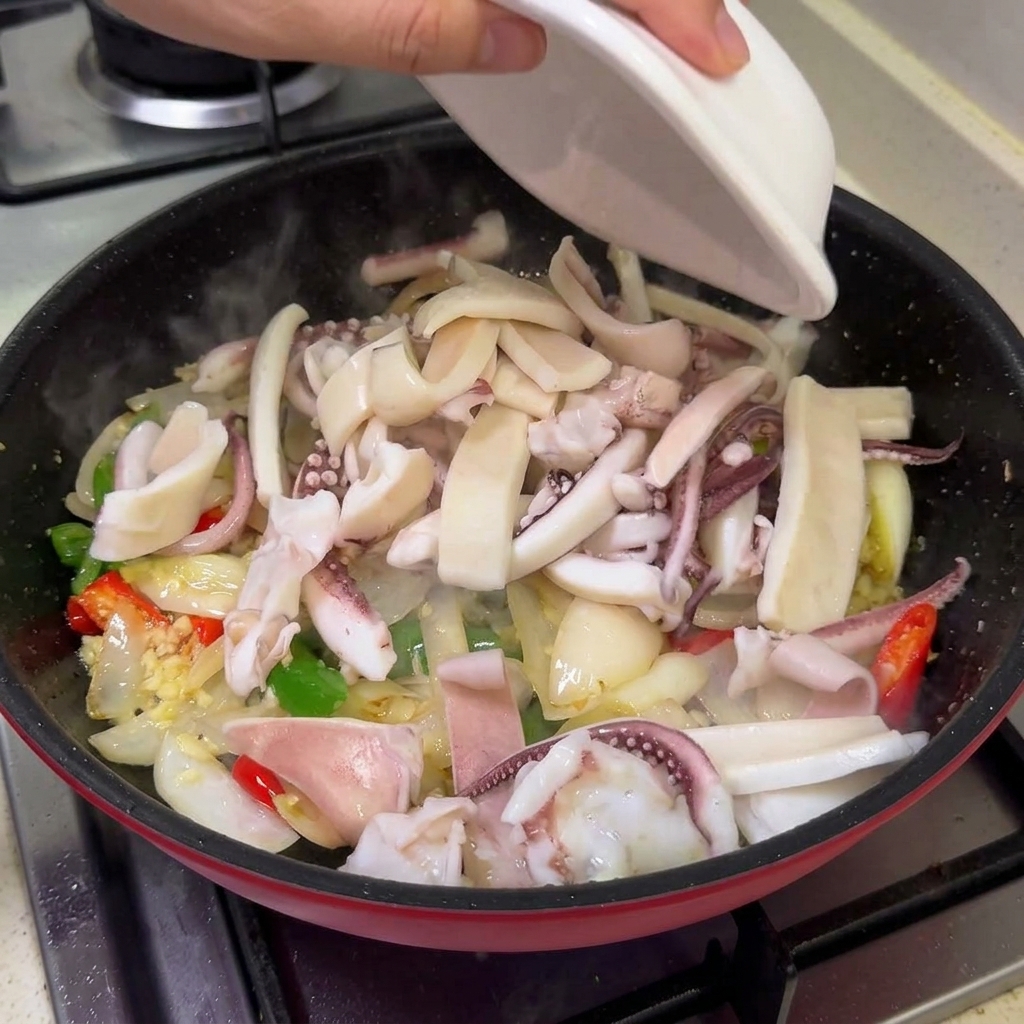 Blanchierter Tintenfisch und Schweinebauch werden aus einer Schüssel zu dem pfannengerührten Gemüse in die Pfanne gegeben.