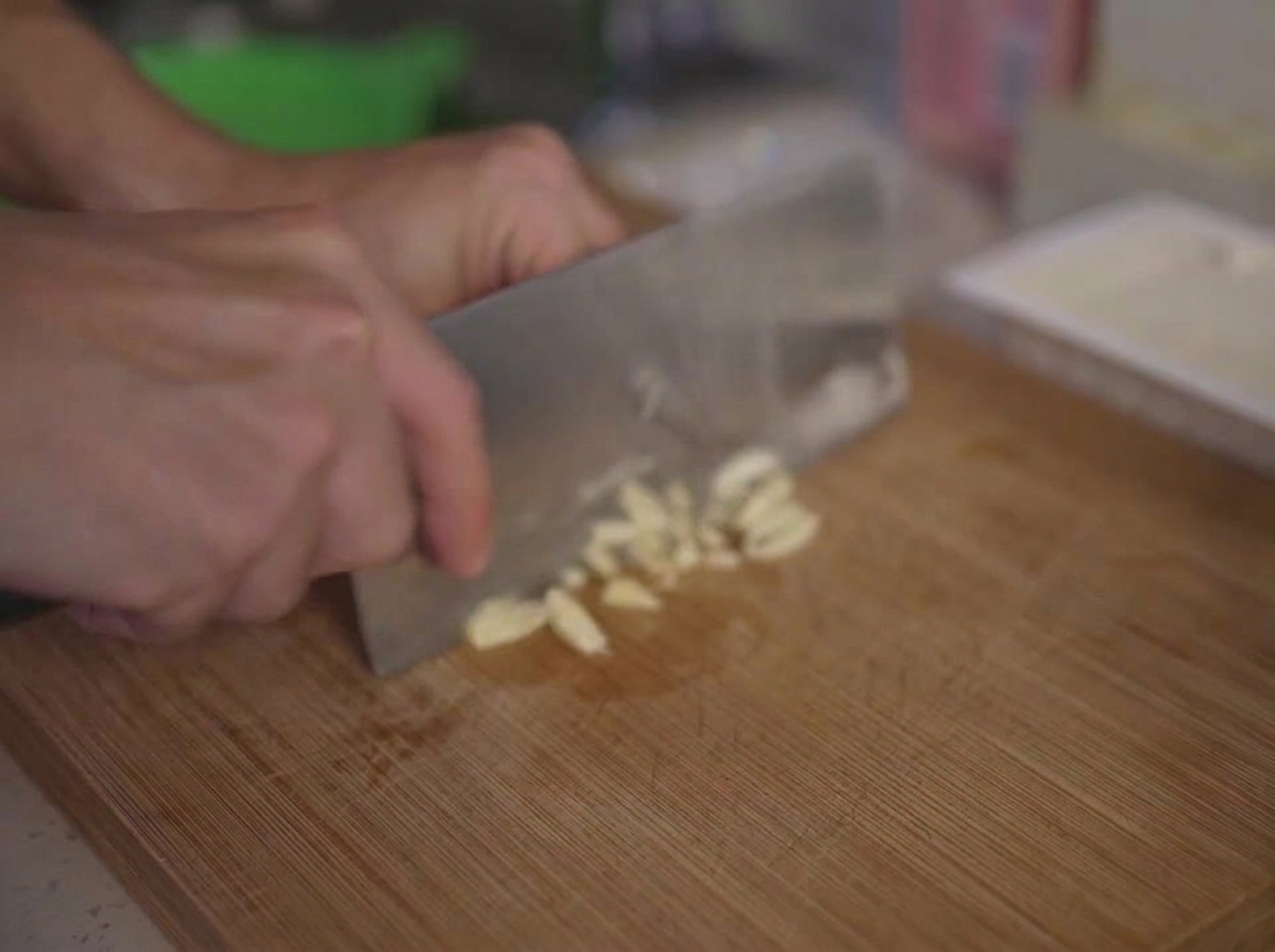 Fein gehackte Knoblauchzehen auf einem Holzschneidebrett neben einem Küchenmesser.