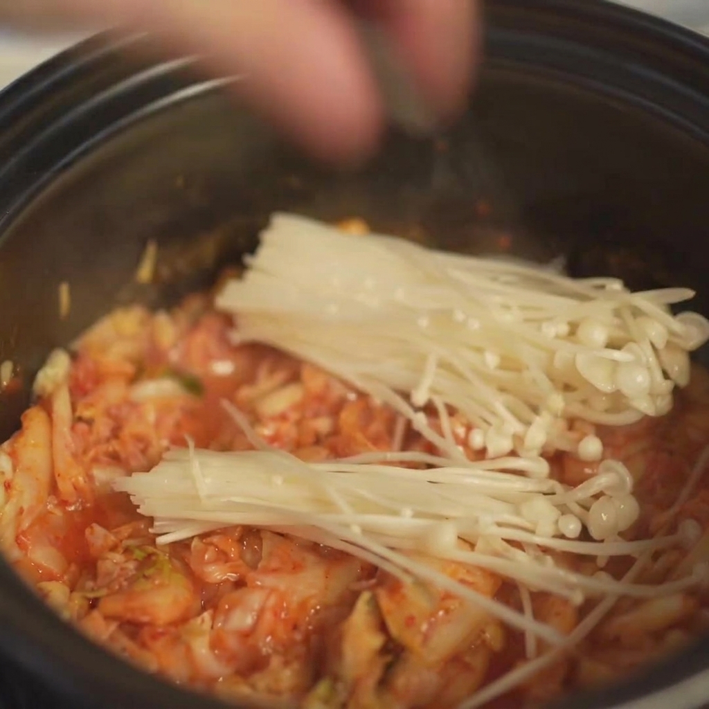 Ein Bund frische Enoki-Pilze wird im Topf auf der angebratenen Kimchi-Schicht platziert.