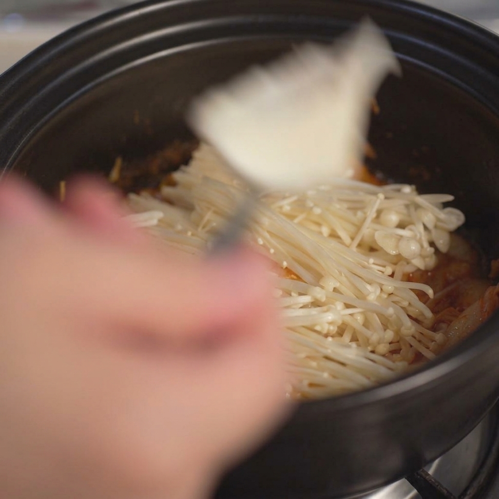 Große Stücke von weichem, weißem Tofu werden mit einem Löffel in den Topf gegeben.