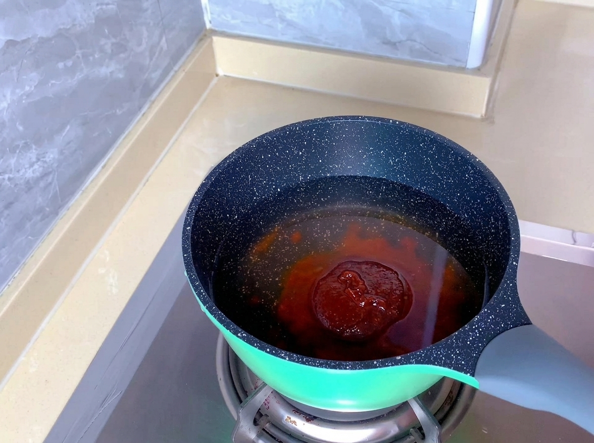 Eine rötlich-orangefarbene Kimchi-Gewürzpaste liegt im klaren Wasser in einem gesprenkelten Topf.