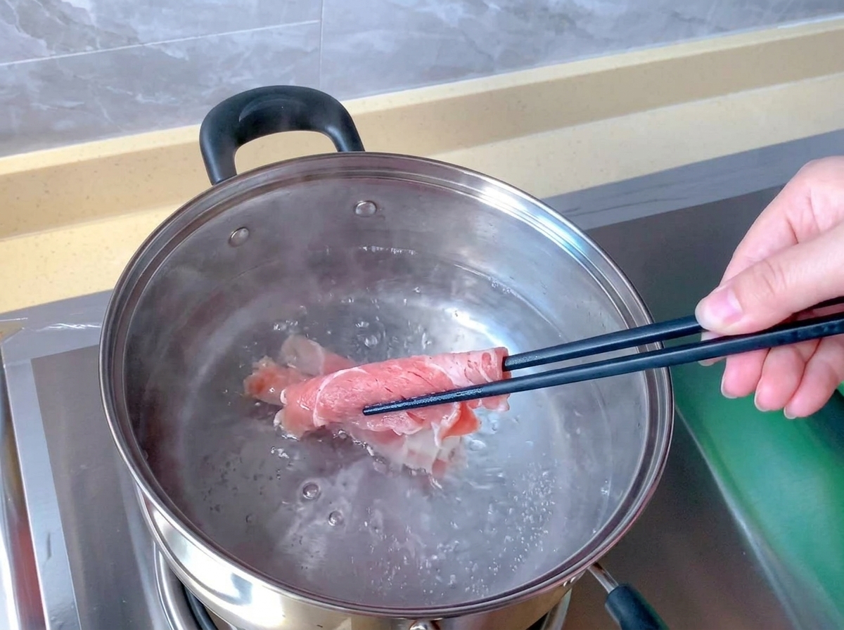 Essstäbchen tauchen ein rohes, rosa Rindfleischröllchen in einen Edelstahltopf mit kochendem Wasser.