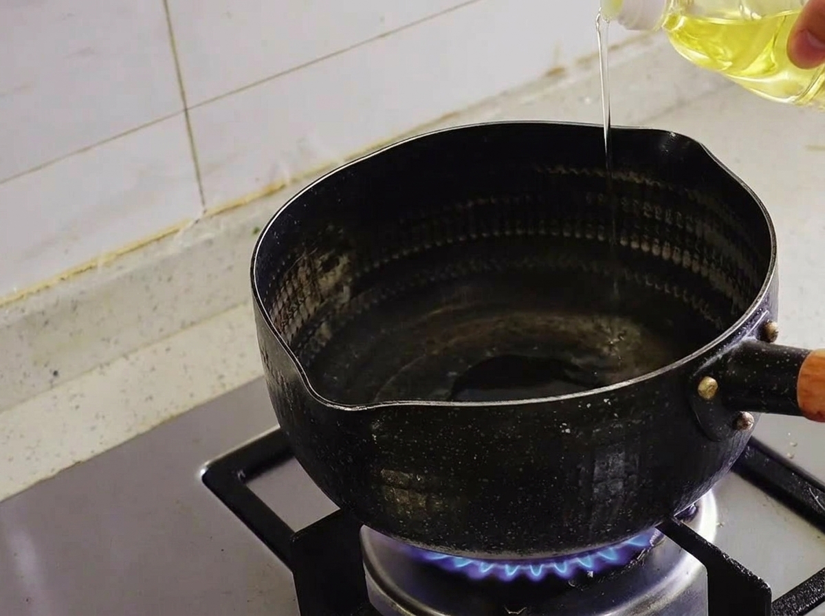 Klares Pflanzenöl wird aus einer Flasche in einen schwarzen Topf auf dem Gasherd gegossen.