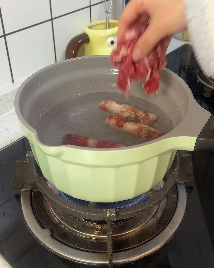 Rindfleischröllchen werden in einem hellgrünen Topf mit kochendem Wasser blanchiert.