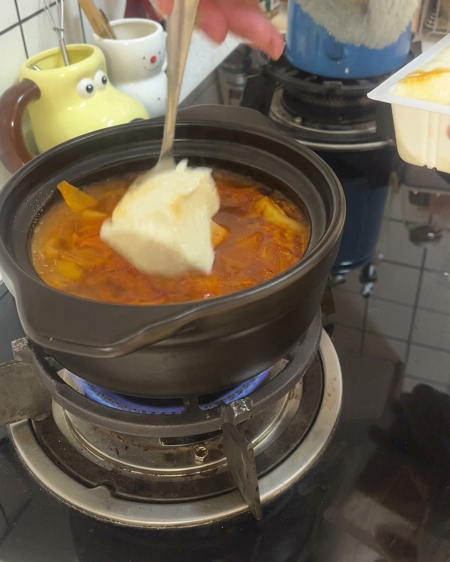 Ein Löffel gibt große Stücke Seidentofu in die kochende rote Brühe im Tontopf.