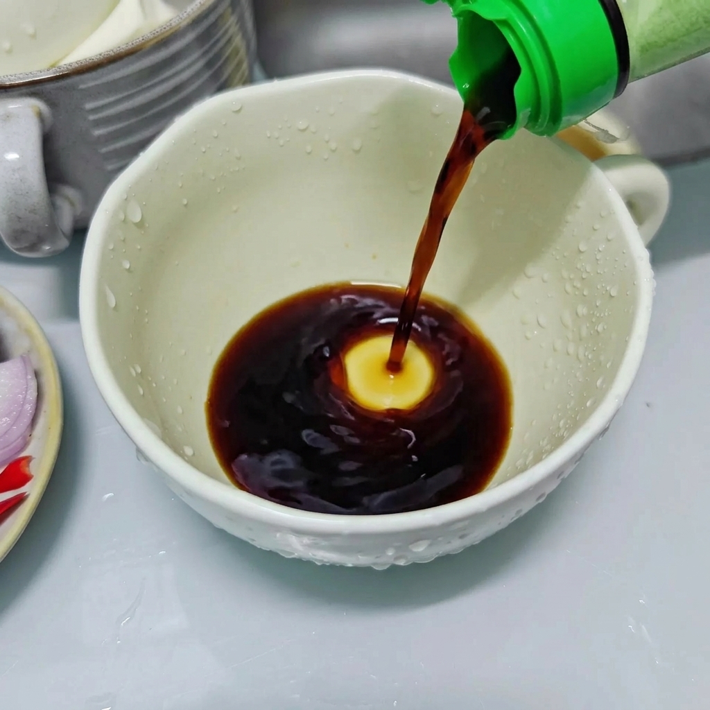 Dunkle Sojasauce wird aus einer Flasche mit grünem Deckel in eine weiße Keramiktasse gegossen, um die Würzsauce vorzubereiten.