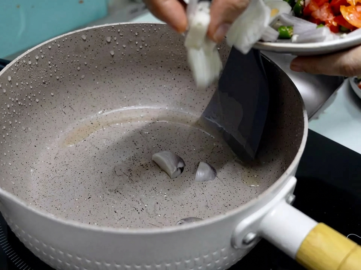 Eine Hand lässt frisch geschnittene rote Zwiebeln von einem kleinen Teller in eine erhitzte, beschichtete Pfanne mit heißem Speiseöl gleiten.
