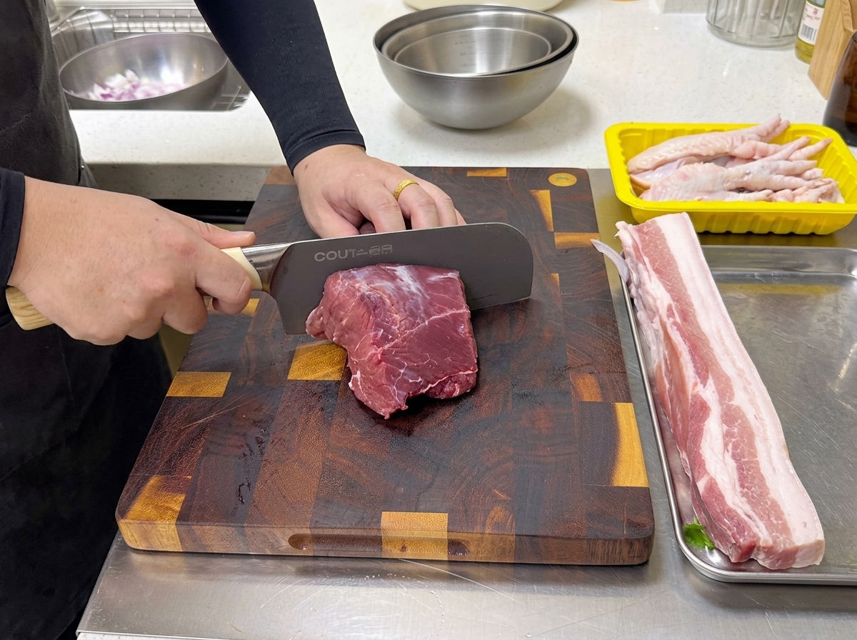 Ein Koch schneidet ein Stück rohes Rindfleisch auf einem Holzschneidebrett mit einem großen Profimesser.