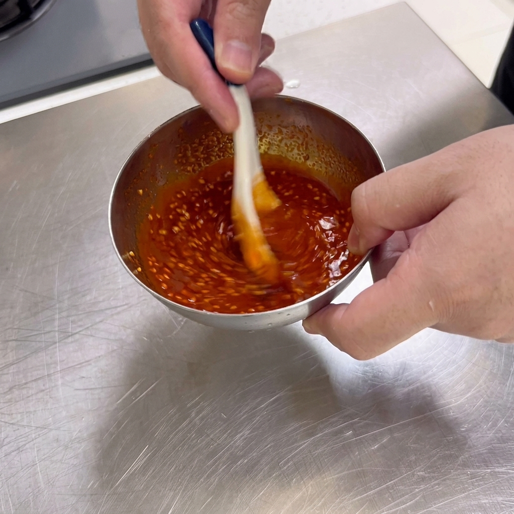 Eine dicke, tiefrote Grill-Dipsauce mit Sesamsamen wird mit einem Löffel in einer kleinen Edelstahlschüssel umgerührt.