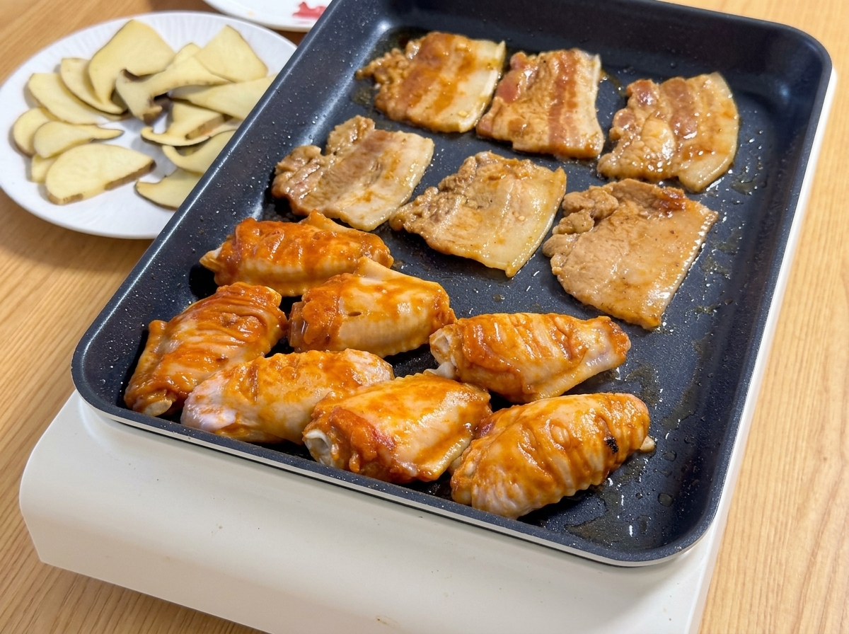 Mariniertes Schweinebauchfleisch und orangefarbene Orleans-Hähnchenflügel braten gemeinsam auf einem heißen Elektrogrill.