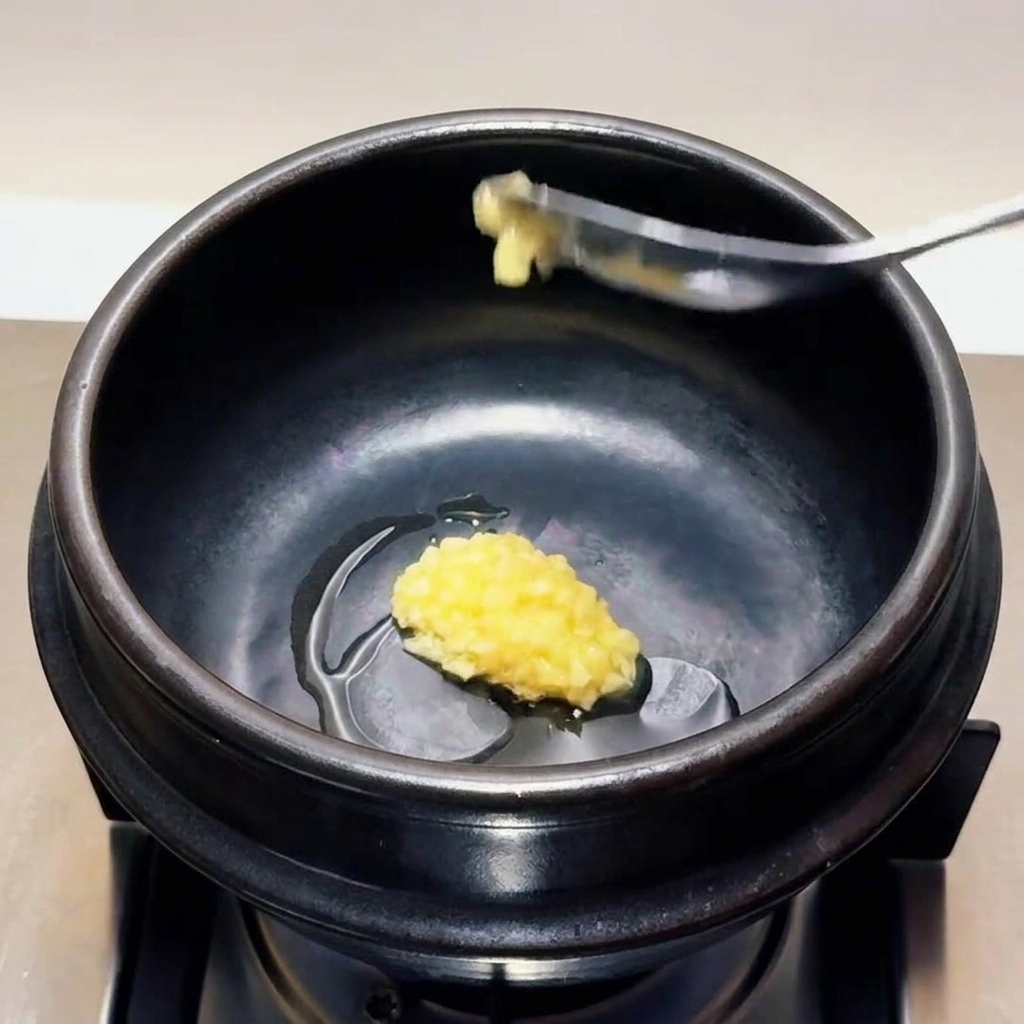 Ein Löffel feingehackter Knoblauch wird in das erhitzte Öl in einem schwarzen Steintopf gegeben.