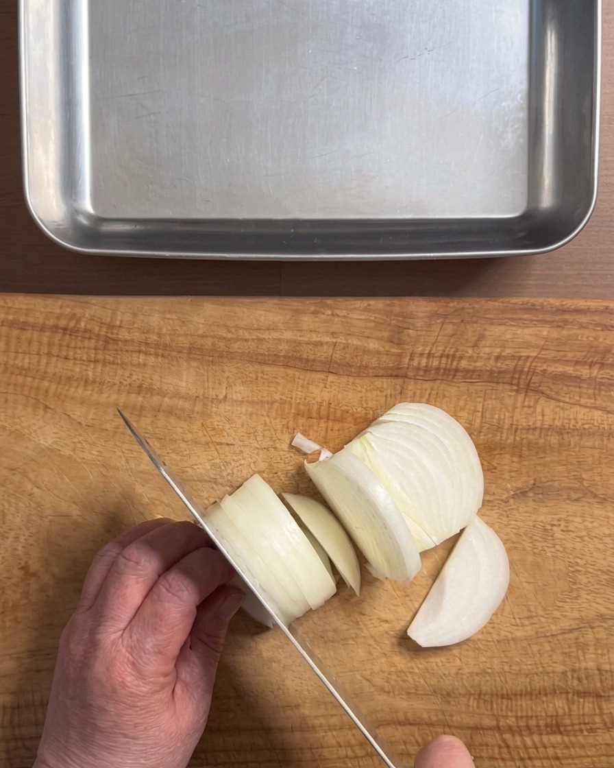 Hände schneiden eine weiße Zwiebel mit einem Messer auf einem Holzschneidebrett in dicke Streifen.