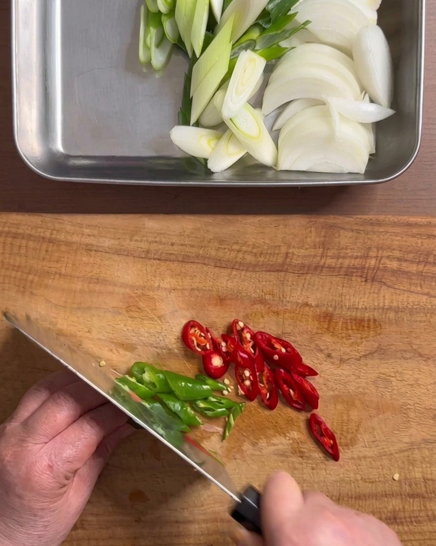 Hände schneiden mit einem Messer grüne und rote Chilischoten auf einem Holzschneidebrett in Ringe.