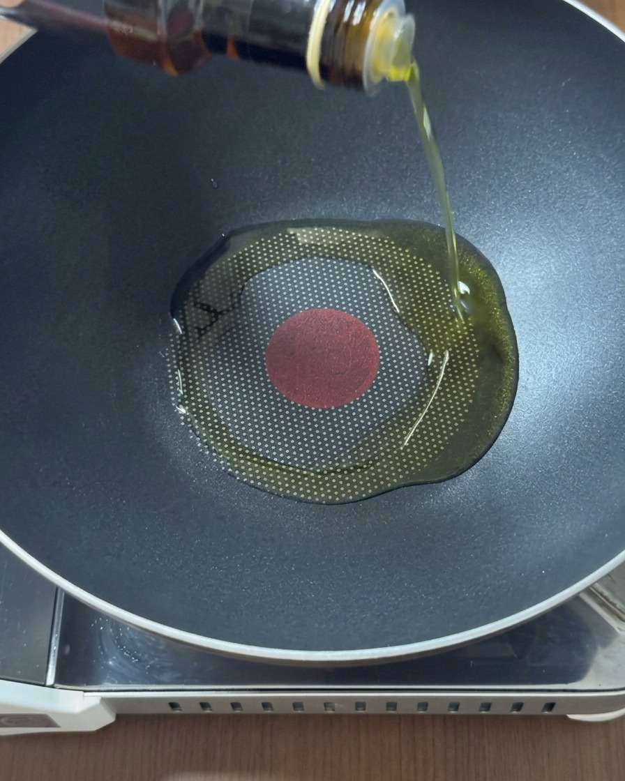Goldenes Öl wird aus einer Glasflasche in die Mitte eines erhitzten schwarzen Woks gegossen.
