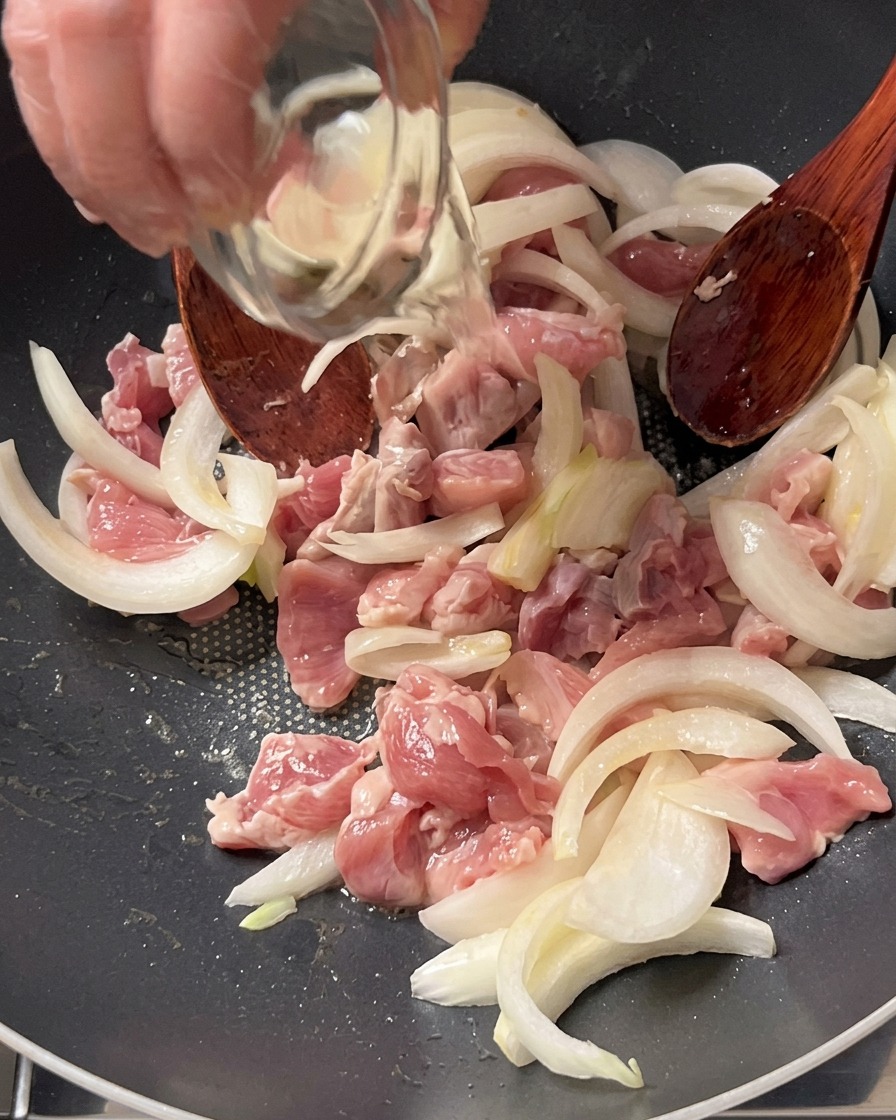 Kochwein wird aus einer kleinen Glasschüssel über Schweinefleisch und Zwiebeln in einer Pfanne gegossen.