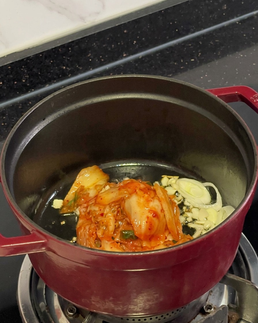 Gehacktes rotes Kimchi, Knoblauchscheiben und Frühlingszwiebeln braten in Öl in einem Topf.