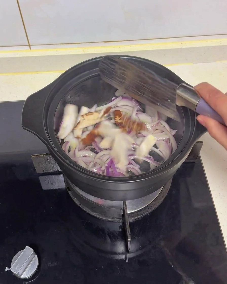 Geschnittene Shiitake-Pilze werden mit einem Pfannenwender zusammen mit den roten Zwiebeln in einem schwarzen Topf angebraten.
