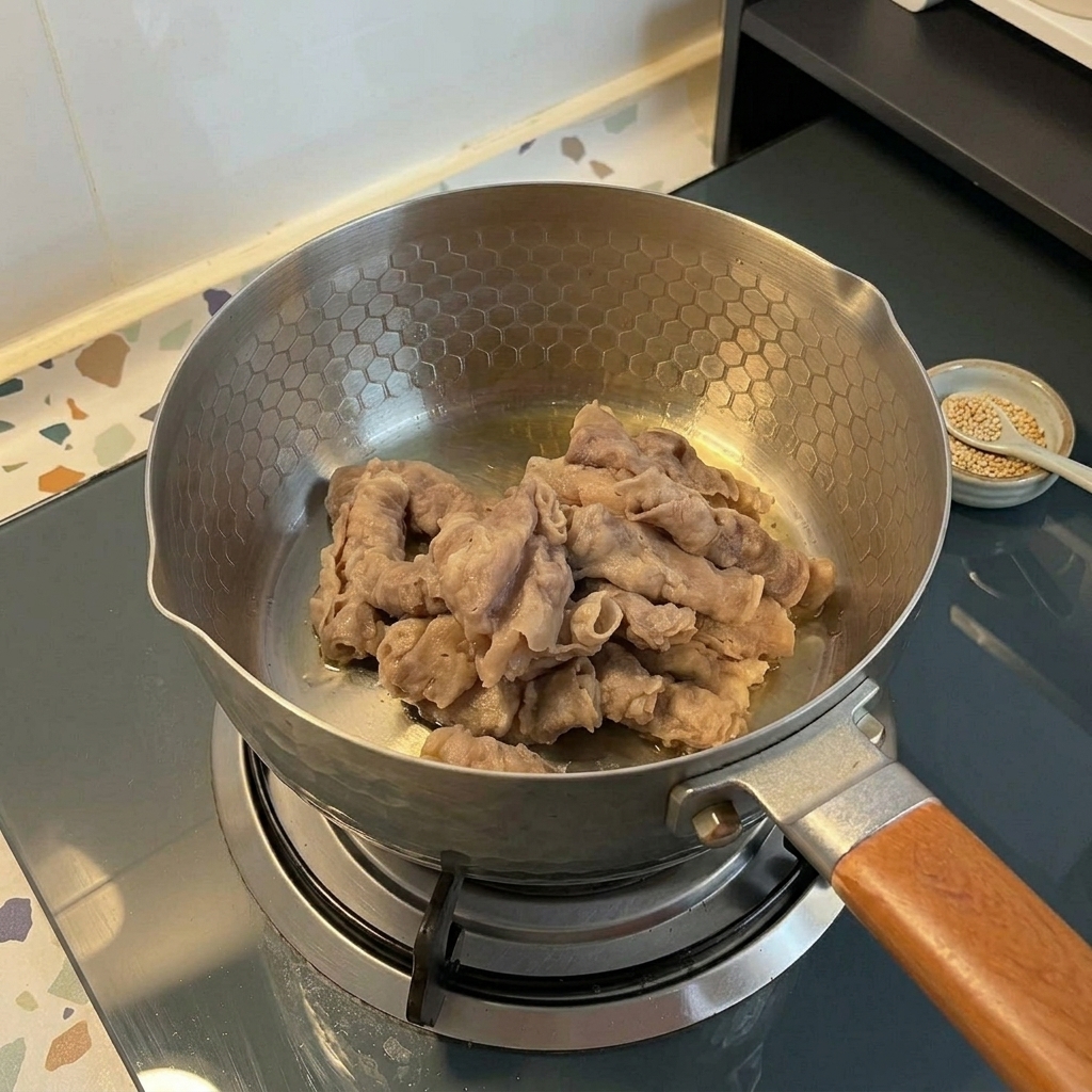 In Streifen geschnittenes Rindfleisch wird in einem Edelstahltopf mit Wabenmuster auf einem Gasherd angebraten.