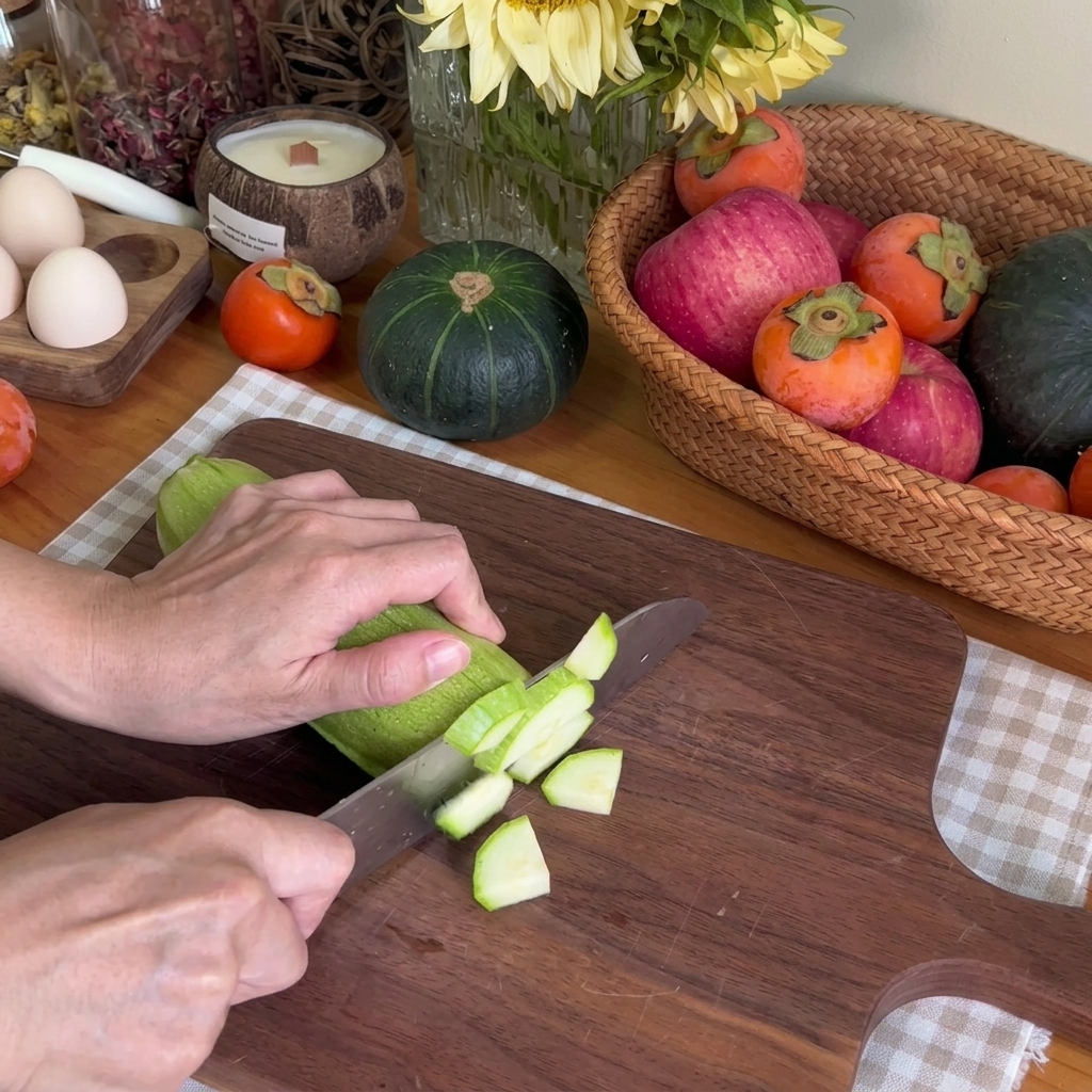 Eine Nahaufnahme von Händen, die eine grüne Zucchini mit einem Kochmesser auf einem Holzschneidebrett in kleine Stücke schneiden.