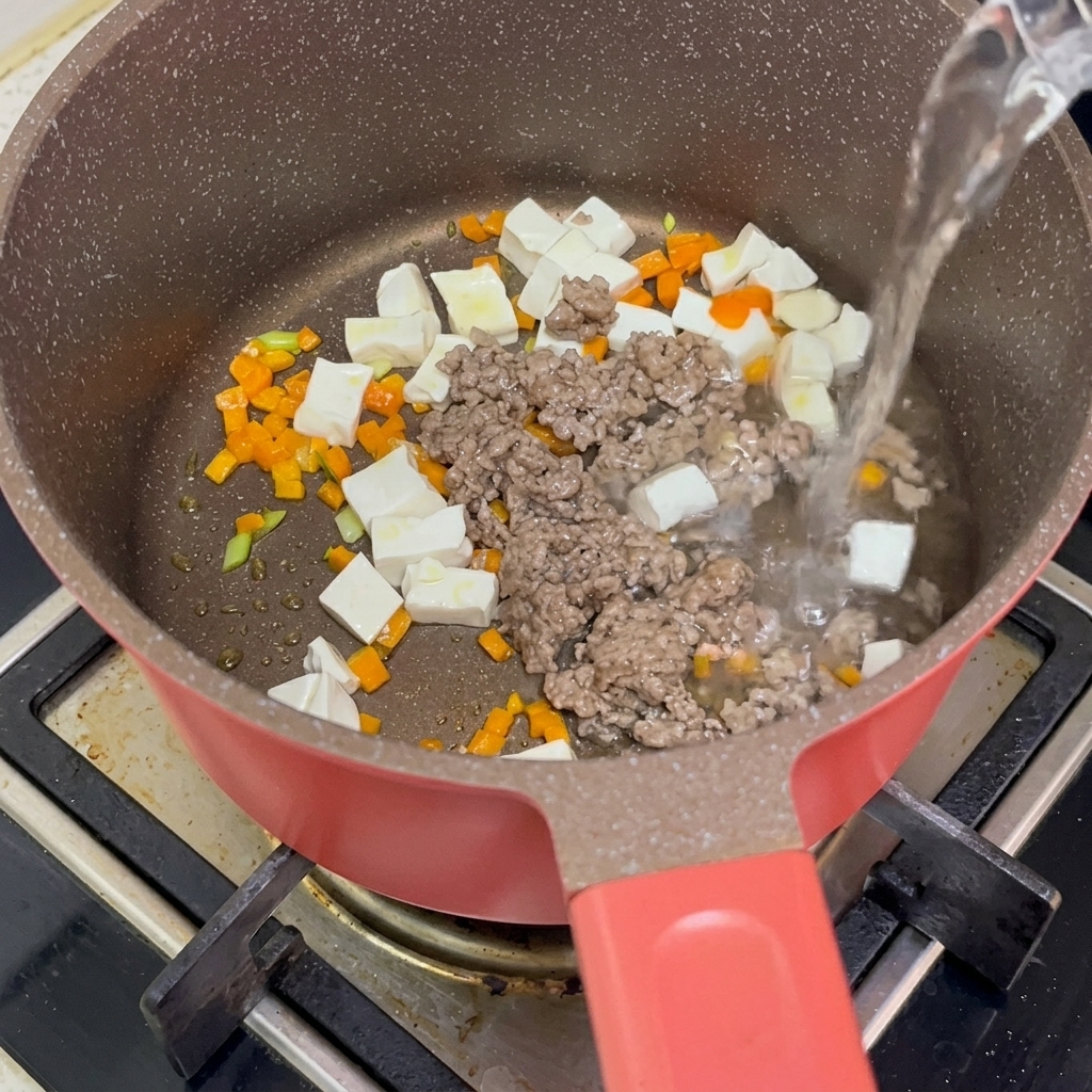 Blanchierte Tofuwürfel, angebratenes Rinderhackfleisch und Karottenwürfel im Topf, während heißes Wasser über die Zutaten gegossen wird.