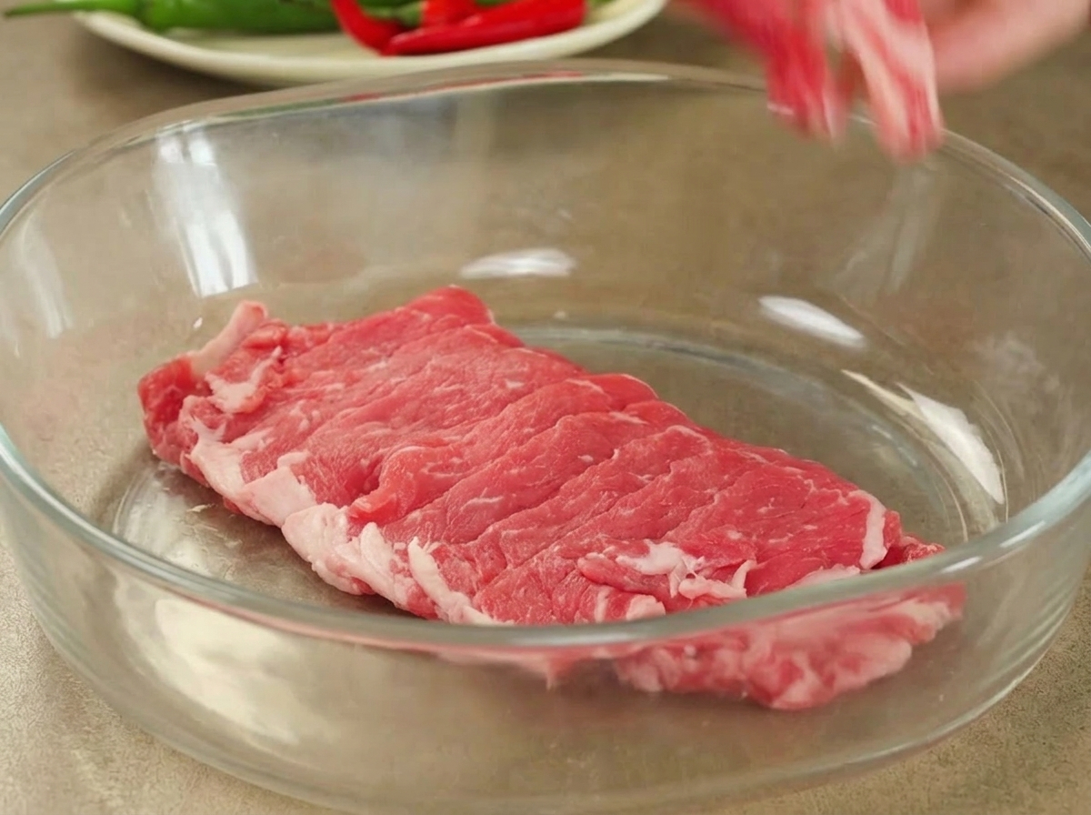 Frisch geschnittenes rohes Rindfleisch, ordentlich in einer großen, klaren Glasschüssel für die Marinade angerichtet.