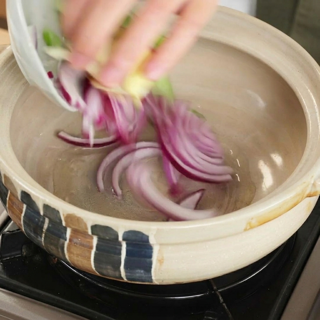 Rote Zwiebelscheiben und andere frische Aromaten werden in einen erhitzten Tontopf gegeben.