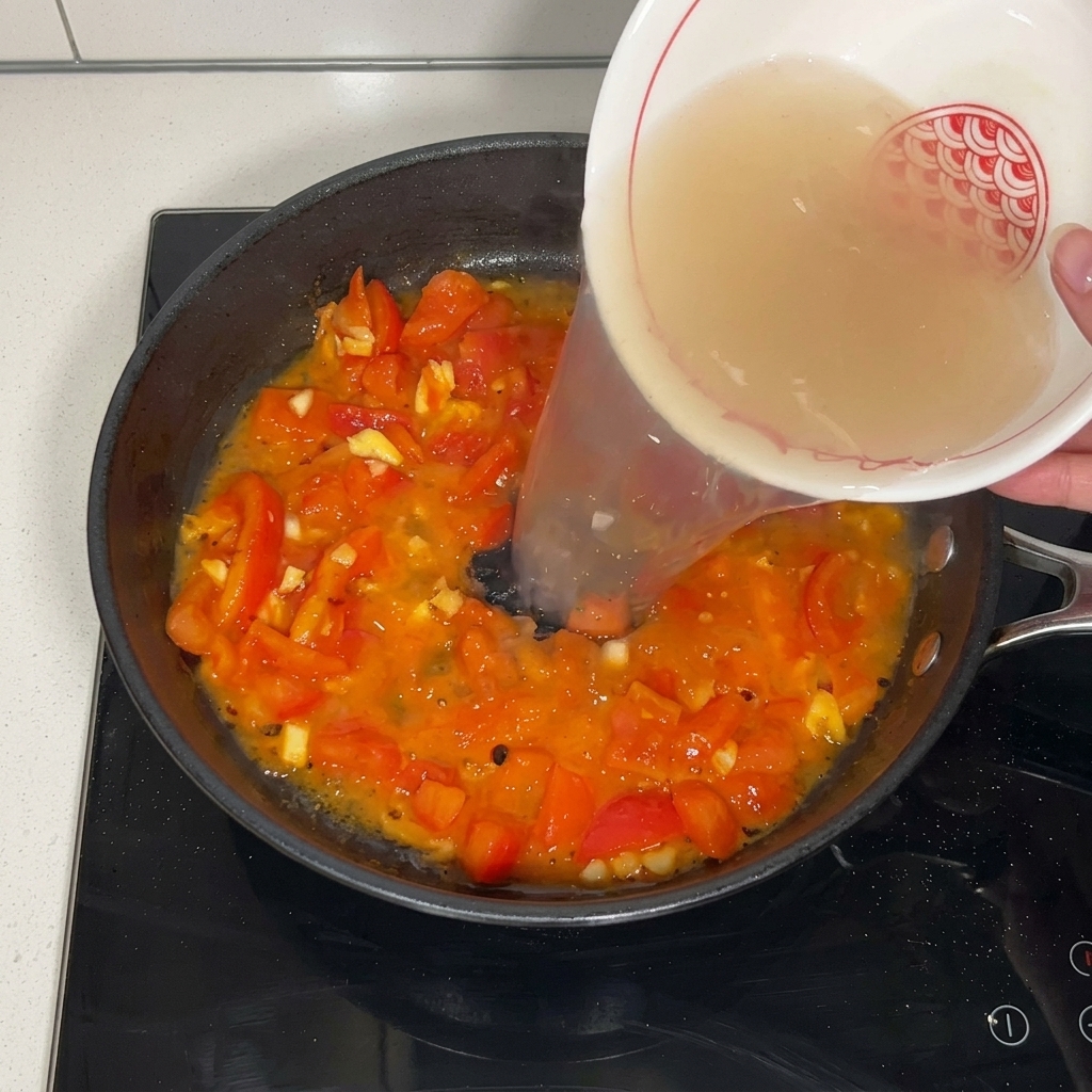Klare Rindfleischbrühe wird aus einer weiß gemusterten Keramikschale in die Pfanne zu den geschmorten Tomaten gegossen.