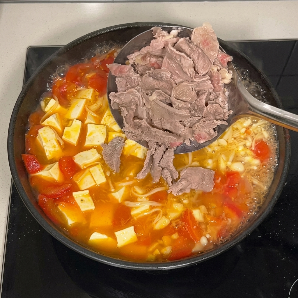 Ein Schaumlöffel gibt die dünnen Scheiben des blanchierten Rindfleischs zurück in die brodelnde Pfanne mit Tomatenbrühe, Enoki-Pilzen und Tofu.