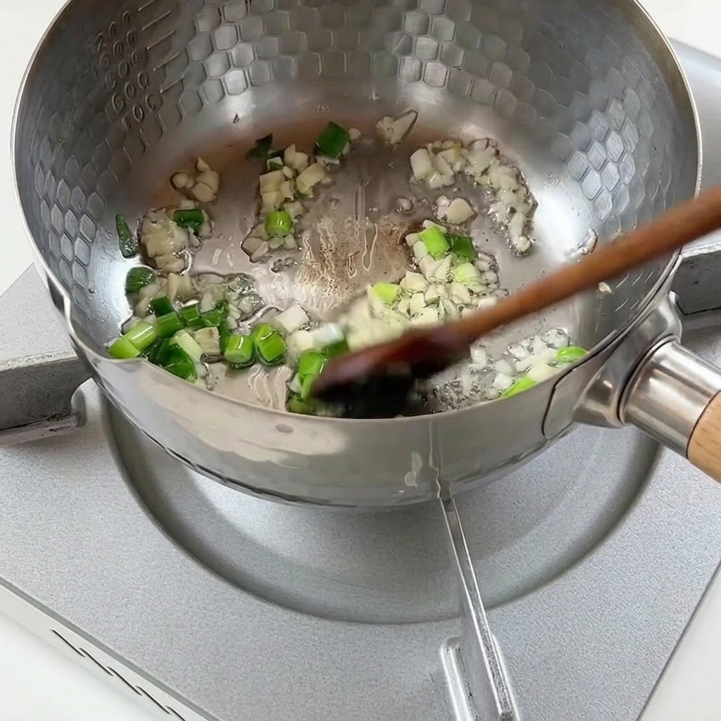Gehackte Frühlingszwiebeln und gehackter Knoblauch braten in heißem Öl in einem strukturierten Metalltopf.