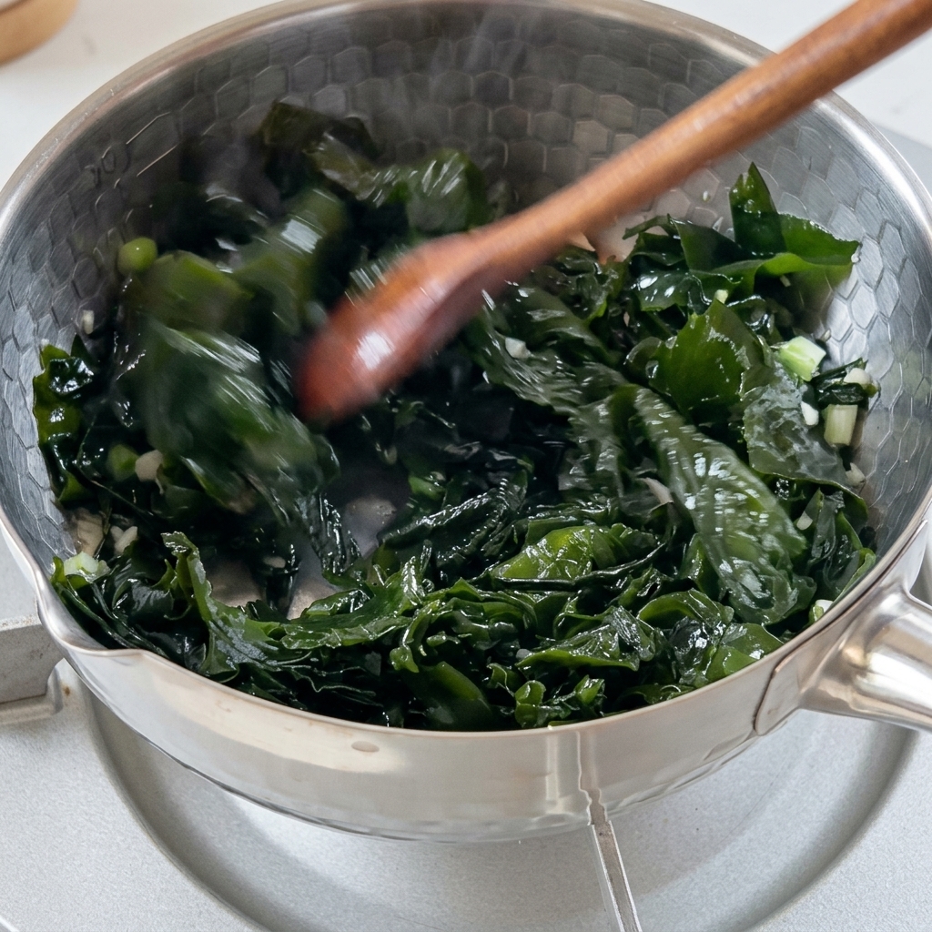 Rehydrierte grüne Wakame-Algen werden mit den Aromaten im Topf verrührt.