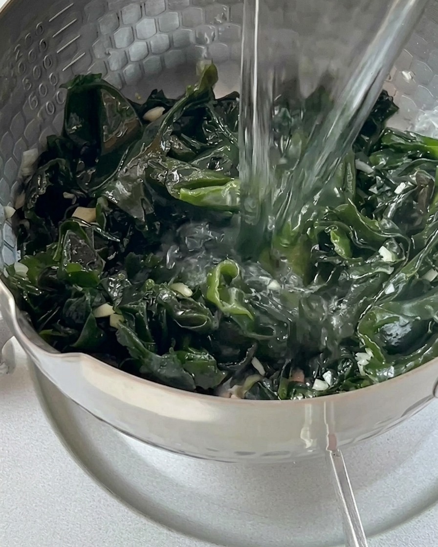 Kochendes Wasser wird aus einem Wasserkocher über die grünen Wakame-Algen im Topf gegossen.