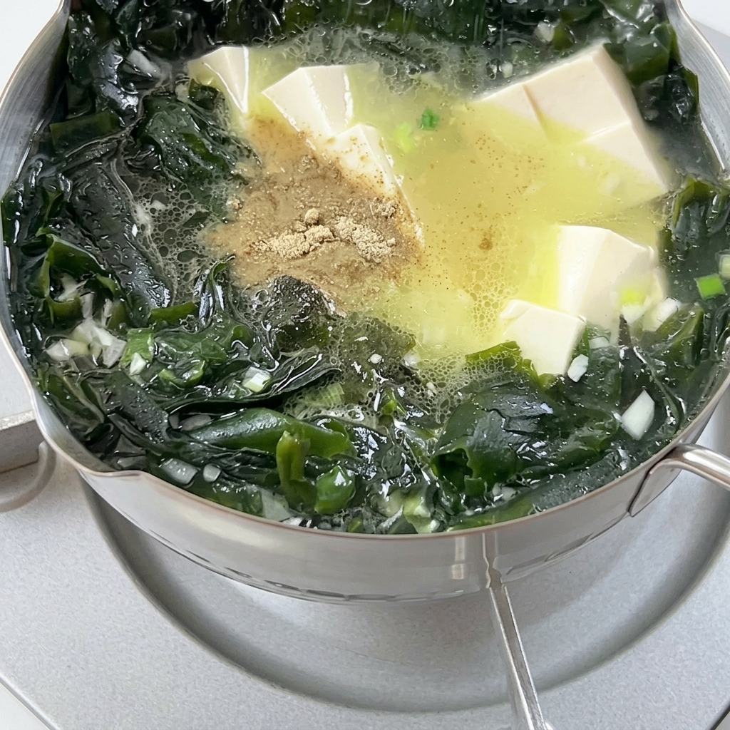 Pfeffer wird in einen Topf mit sprudelnder Suppe aus Wakame-Algen und Tofuwürfeln gestreut.