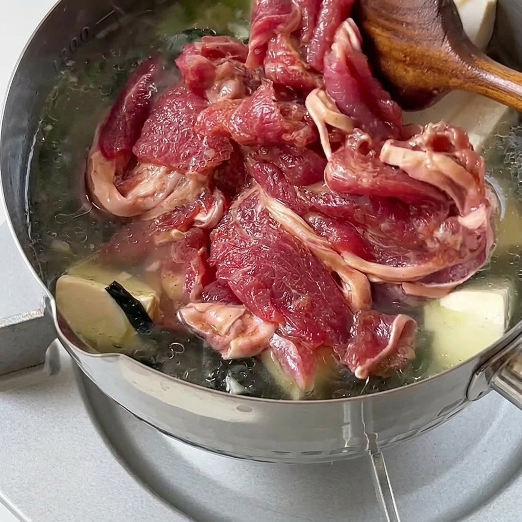 Marinierte rohe Rindfleischscheiben werden vorsichtig in den heißen Topf mit Suppe gegeben.