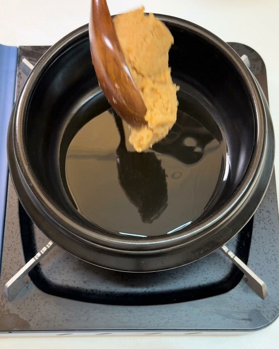 Ein großer Löffel mit Sojabohnenpaste wird in einen Topf mit schimmerndem Sesamöl gegeben.