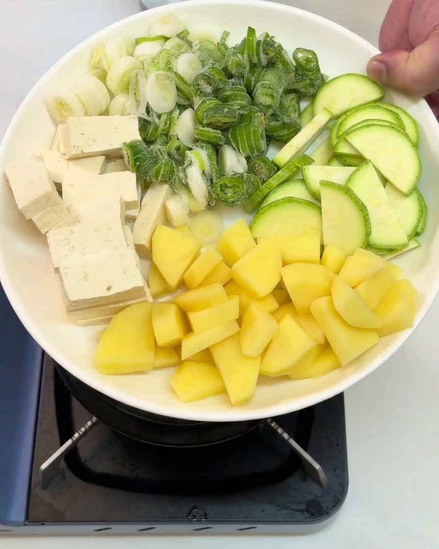 Ein Teller mit gewürfeltem Tofu, Zucchini, Kartoffeln und Frühlingszwiebeln steht bereit.