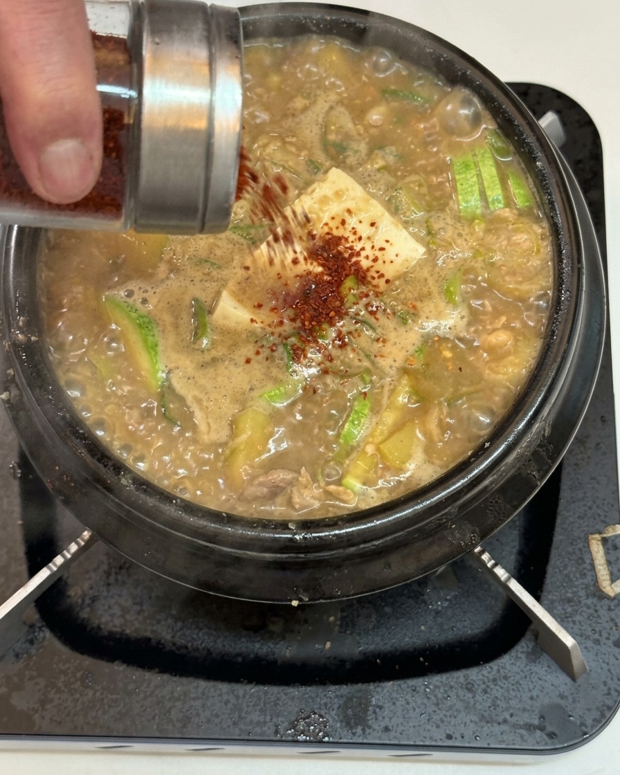 Rotes Chilipulver wird über den kochenden Eintopf gestreut.
