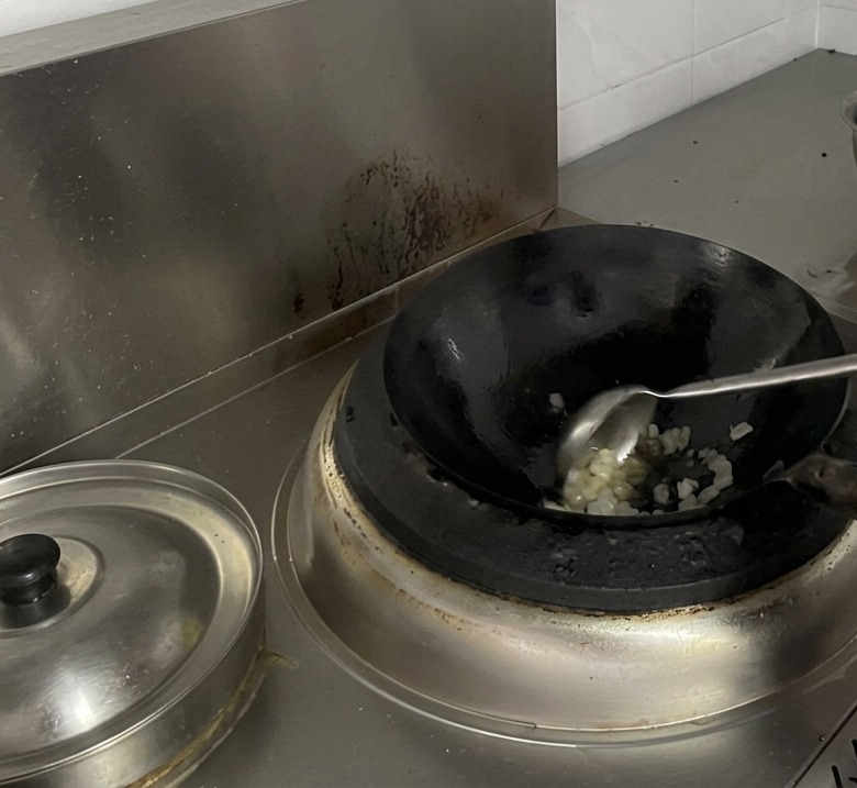 Ein Koch rührt mit einer großen Kelle schmelzenden Kluntenzucker im Wok um.