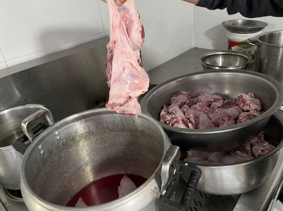 Eine Hand hält ein großes Stück rohes Fleisch und legt es in den Topf zu den Schweinefüßen.