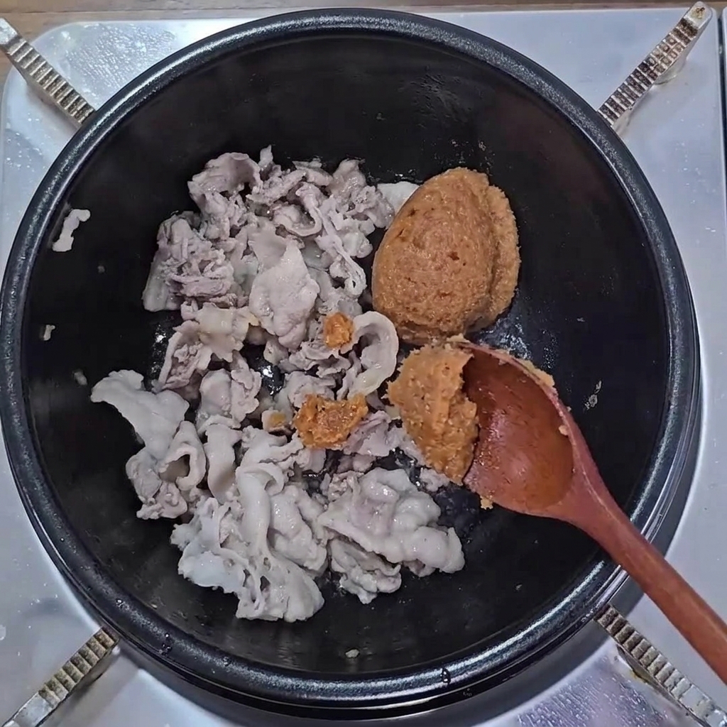 Braune Sojabohnenpaste und Ssamjang werden zu gebratenem Schweinebauch in einem Topf gegeben.