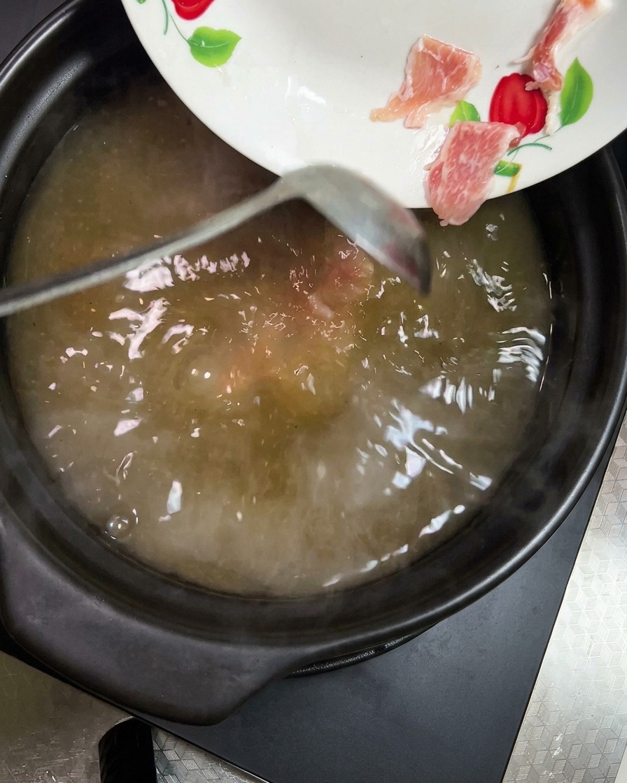 Karotten- und Kartoffelstücke werden in die simmernde Suppe gegeben.