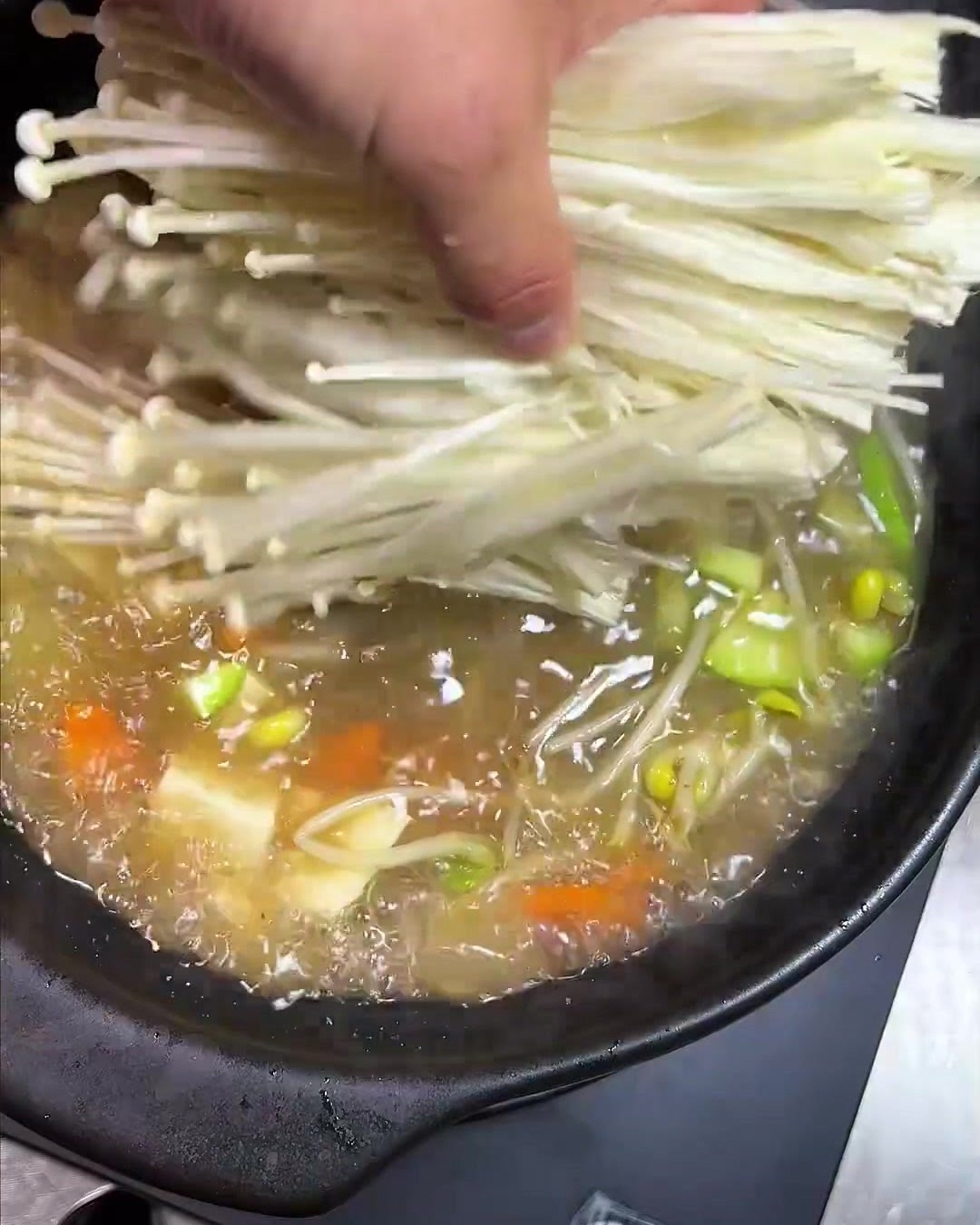 Ein Bündel feiner, langstieliger Enoki-Pilze wird in den Topf gegeben.