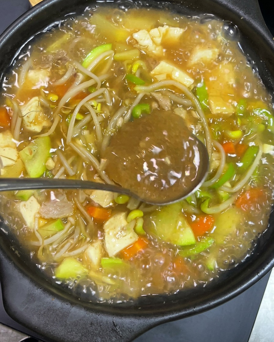 Koreanische Würzpaste wird in den dampfenden Eintopf eingerührt.