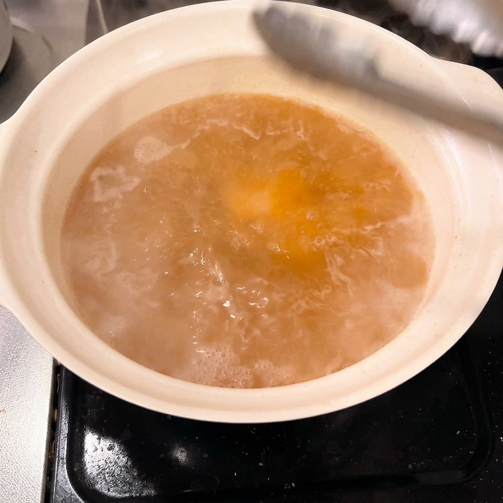 Dicke Stücke blanchierten Schweinebauchs werden vorsichtig in die Miso-Brühe gelegt.