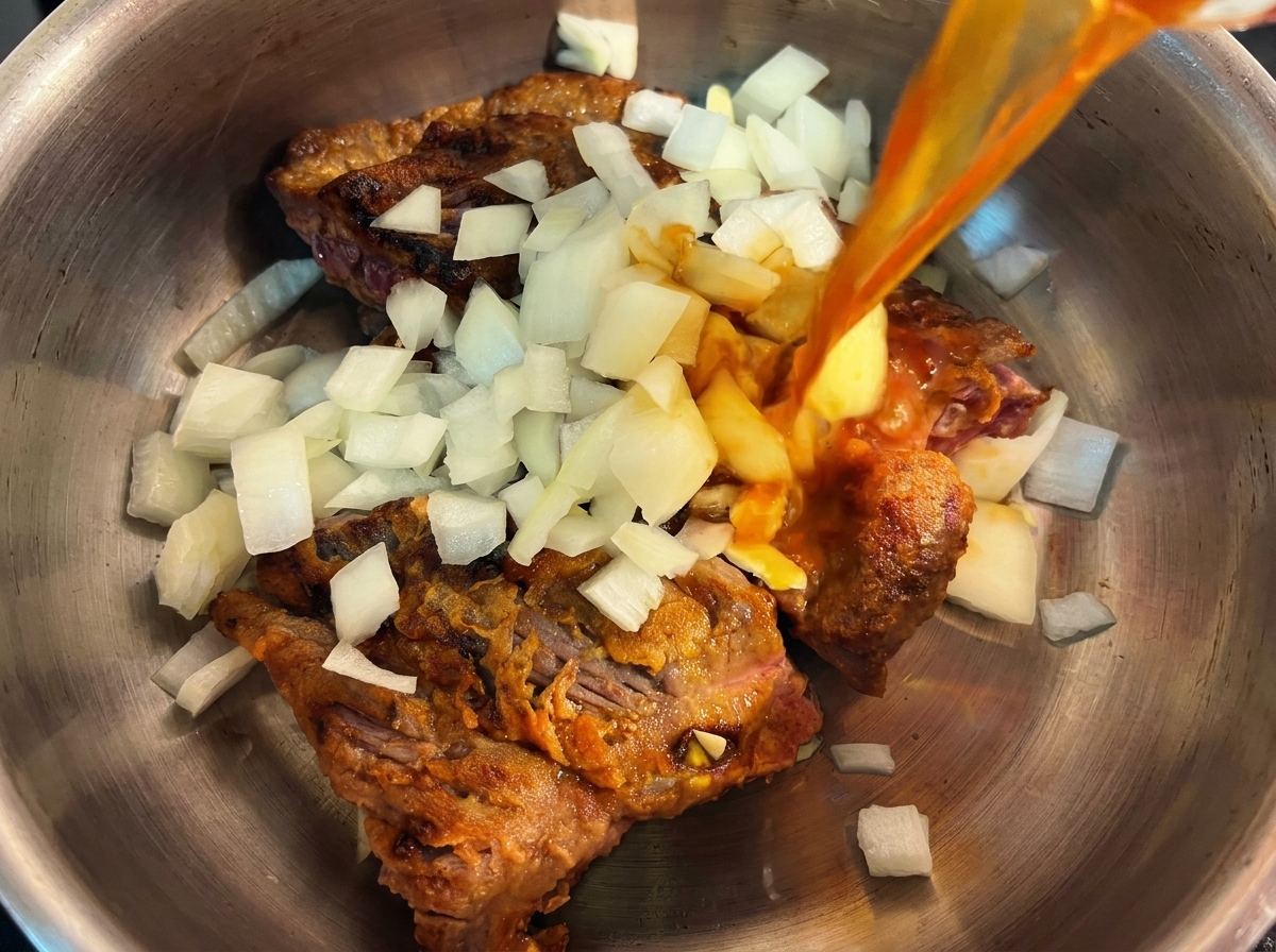 Ein Schnellkochtopf mit angebratenem Rindfleisch und gehackten Zwiebeln, über die eine aromatische Brühe gegossen wird.