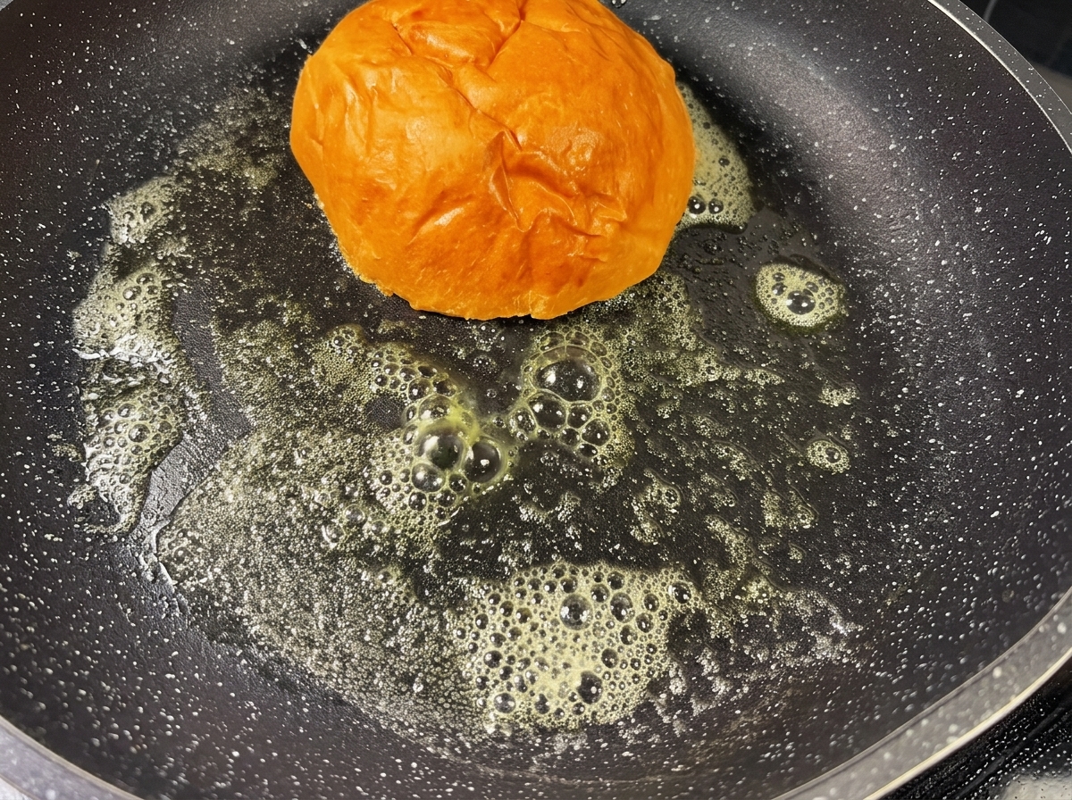 Ein Burgerbrötchen wird in einer heißen Pfanne mit geschmolzener Butter goldbraun angeröstet.