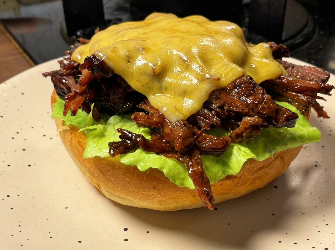 Ein Pulled Beef Burger Patty, belegt mit einer Käsescheibe, die mit einem Flambierbrenner geschmolzen wird.