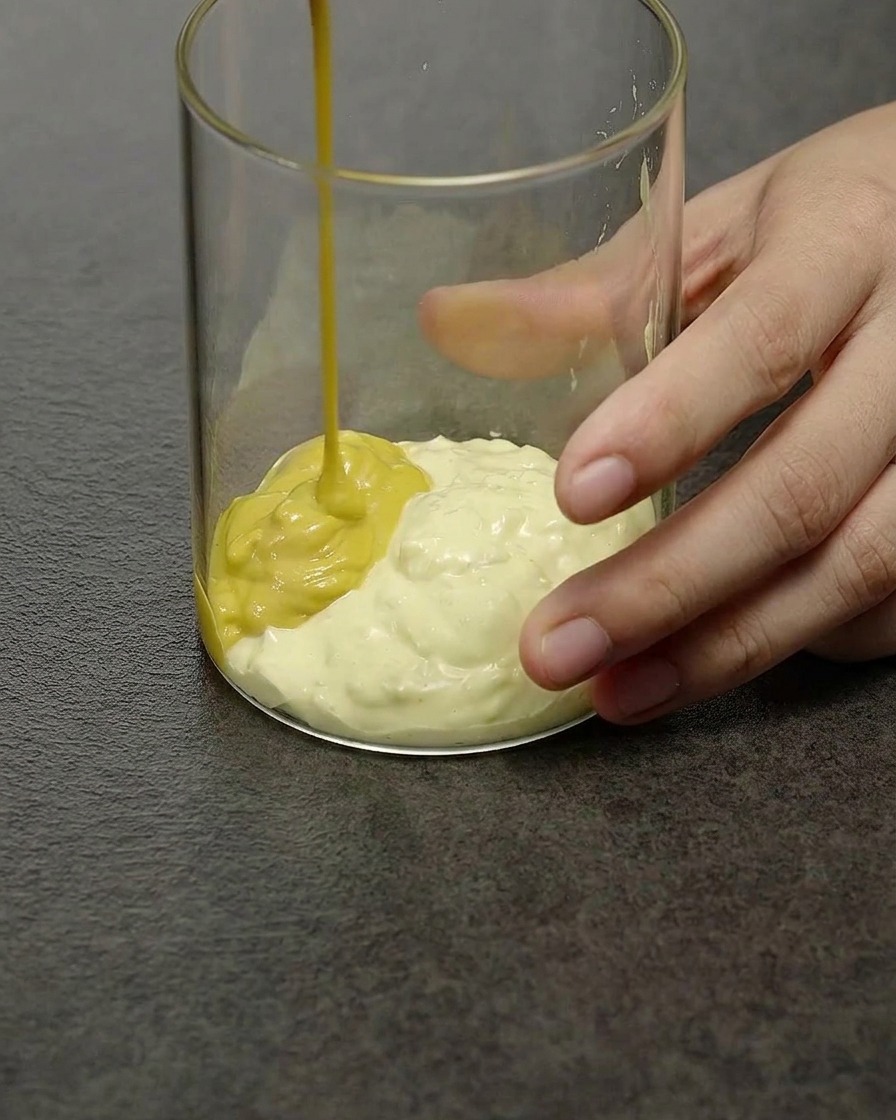 Eine blassgelbe, cremige Burgersauce wird in einem durchsichtigen Glasgefäß umgerührt.