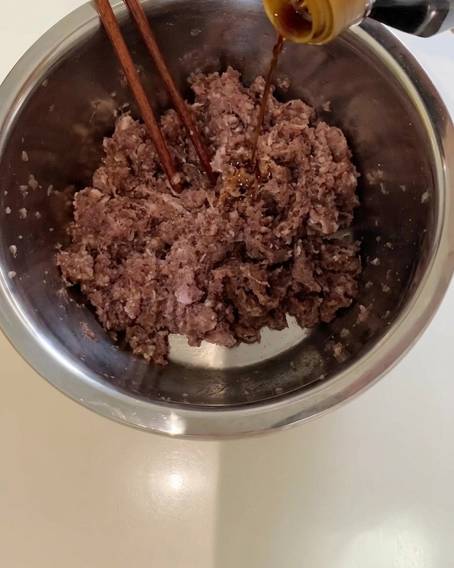 Dunkle Sojasauce wird aus einer Flasche in eine Metallschüssel mit Rinderhackfleisch gegossen.